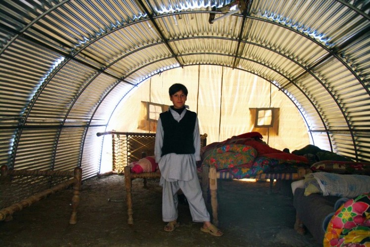 Boy is standing in front of the beds in an emergency shelter.