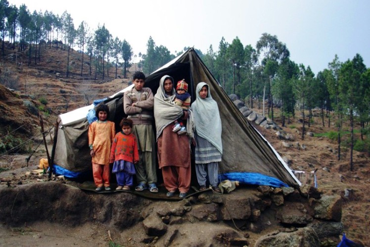 A family of six stands in front of the entrance to their emergency shelter.