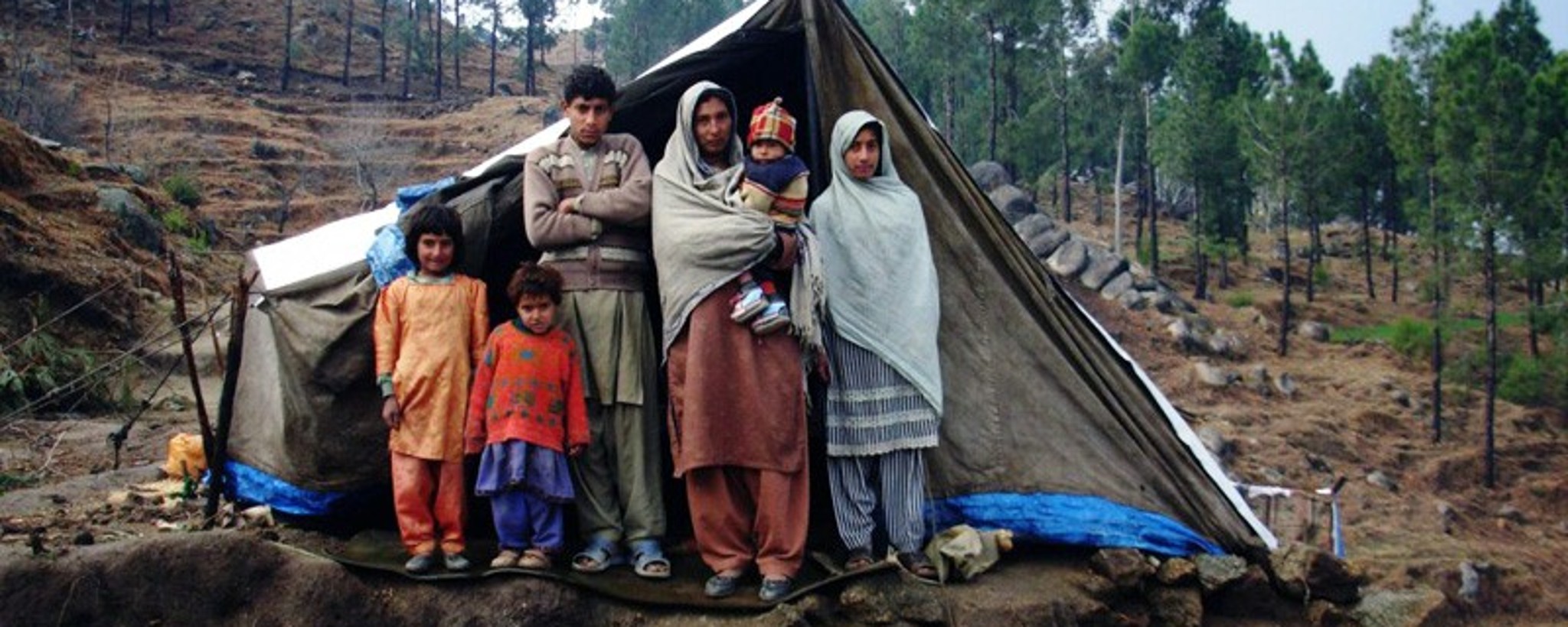 A family of six stands in front of the entrance to their emergency shelter.