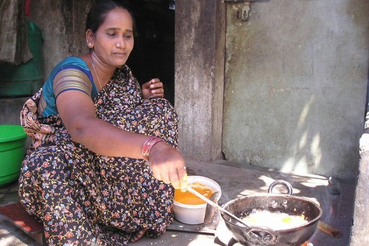 Indian woman sitting in the street cooking food in a pot.