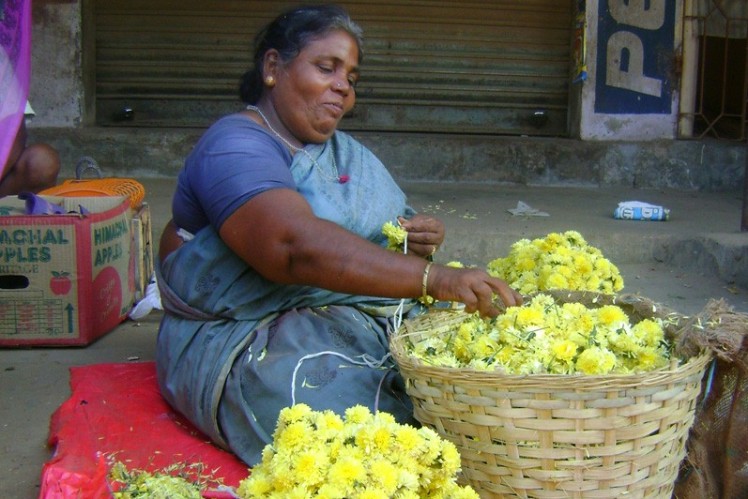 Woman sitting on the street threading flowers on a string.