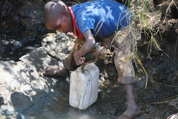 A boy fills his water canister with dirty water from the river.