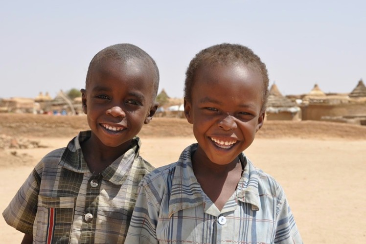 Two boys stand next to each other and laugh into the camera. 