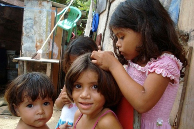 A young girl gets something out of another child's hair.