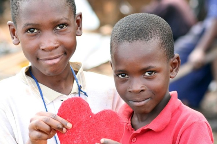 Two boys hold together a red heart in their hands.