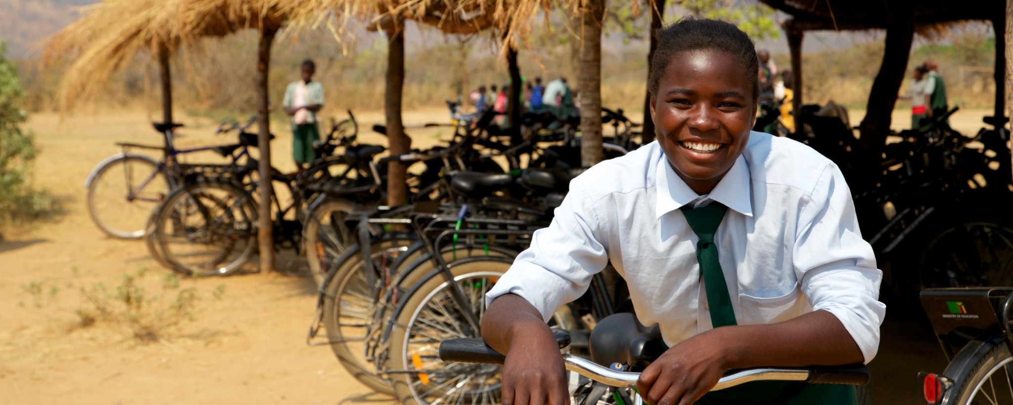 Schoolchild is sitting on his bicycle and is smiling.