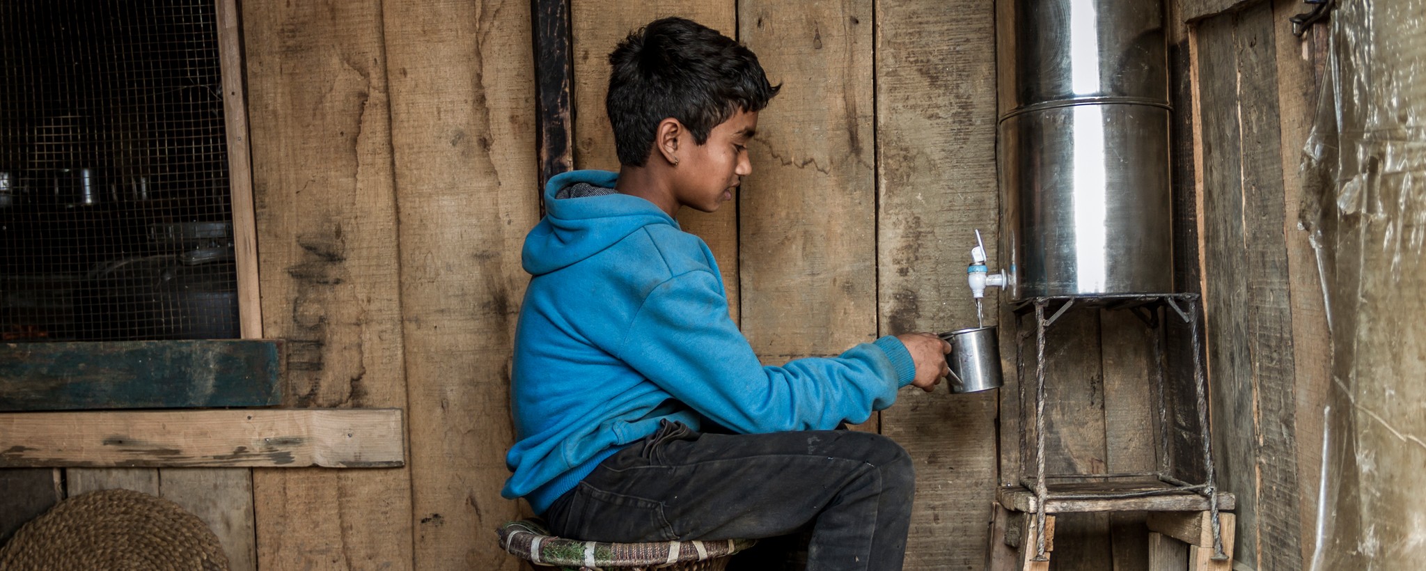 Boy sitting fills his cup with water from the water dispenser.