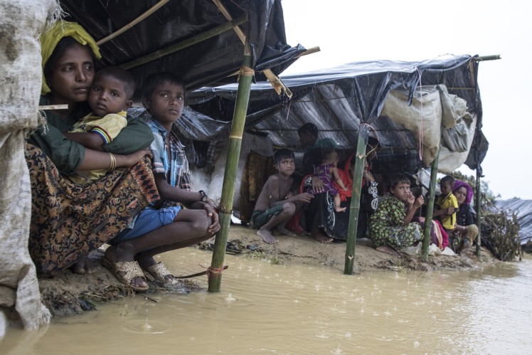 Families sit under a tent and are threatened by flooding.