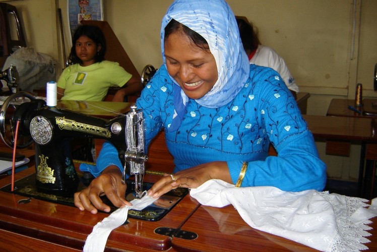 Woman sitting at a sewing machine sewing a skirt.