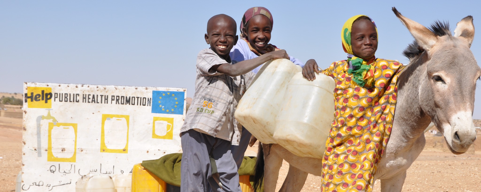 Three African children lean with their water canisters against a donkey.