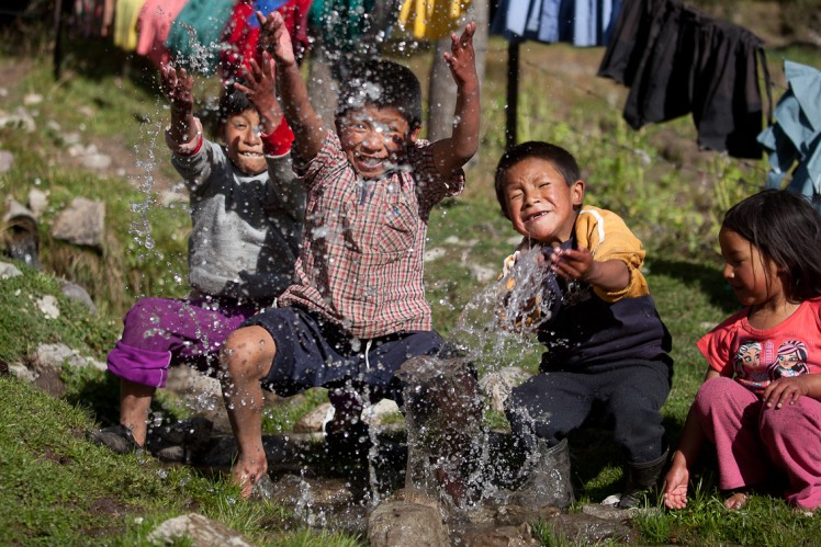 Kinder freuen sich über das fließende Wasser und spritzen es mit ihren Händen in der Gegend herum.