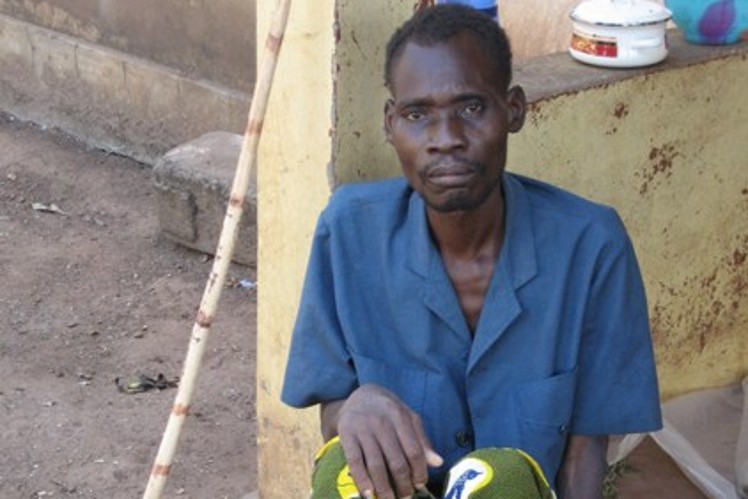 A sick farmer sits in the street alone.