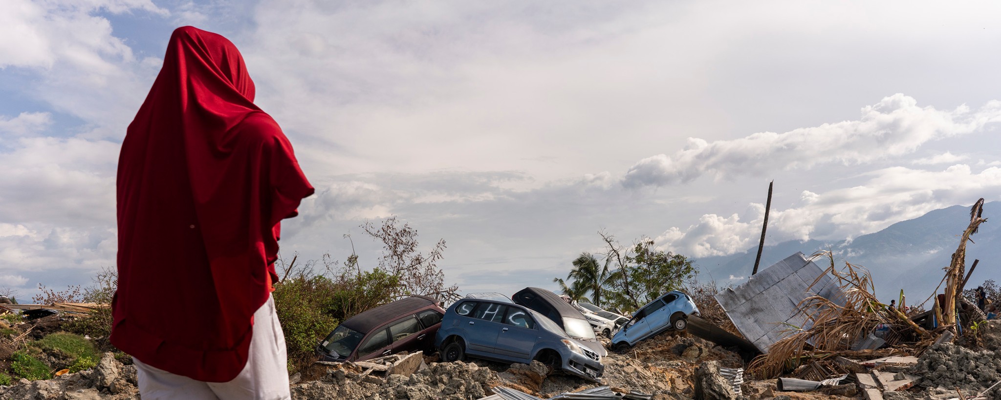 Woman standing in front of a mudslide with destroyed cars.