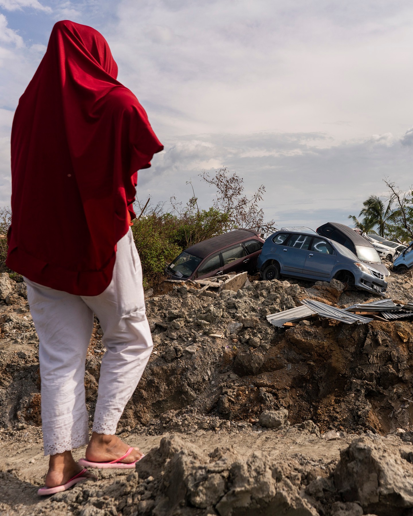 Woman standing in front of a mudslide with destroyed cars.