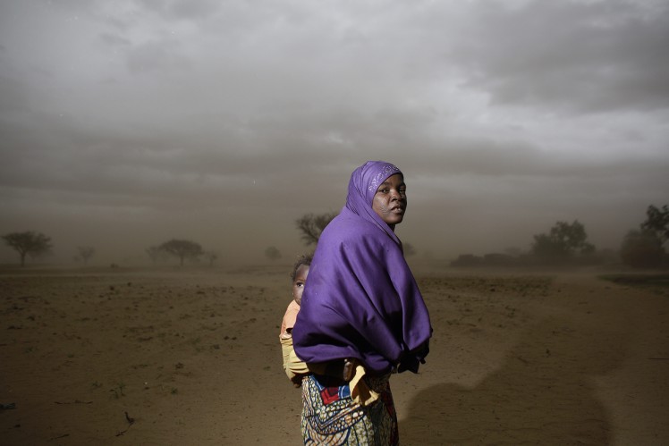 Woman carries her child on her back through the desert.