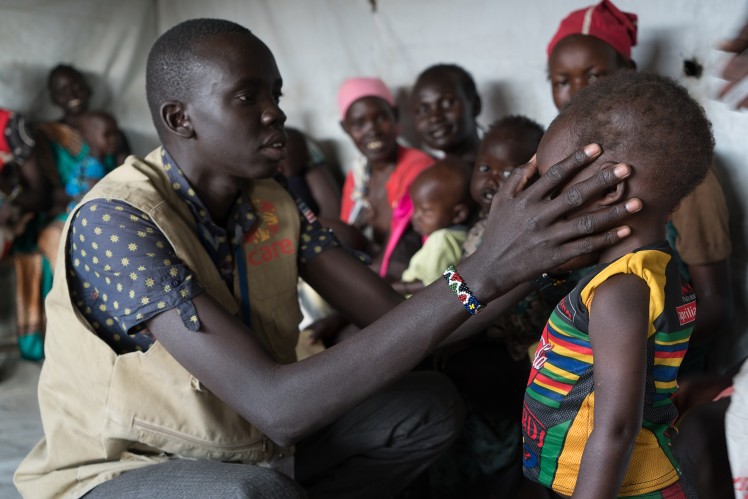 A South Sudanese man, paints with his finger, the sign of the cross on the forehead of a little boy.