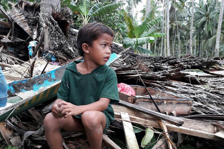 A Filipino boy sits on the ruins of a house.