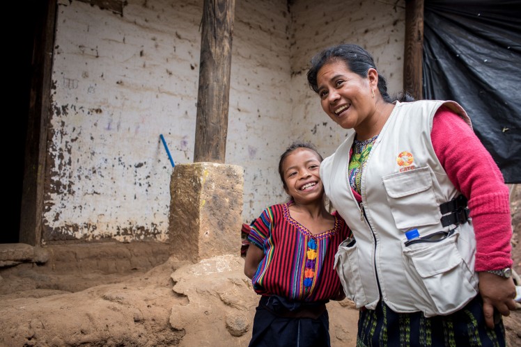 A little girl stands next to a CARE employee and smiles.